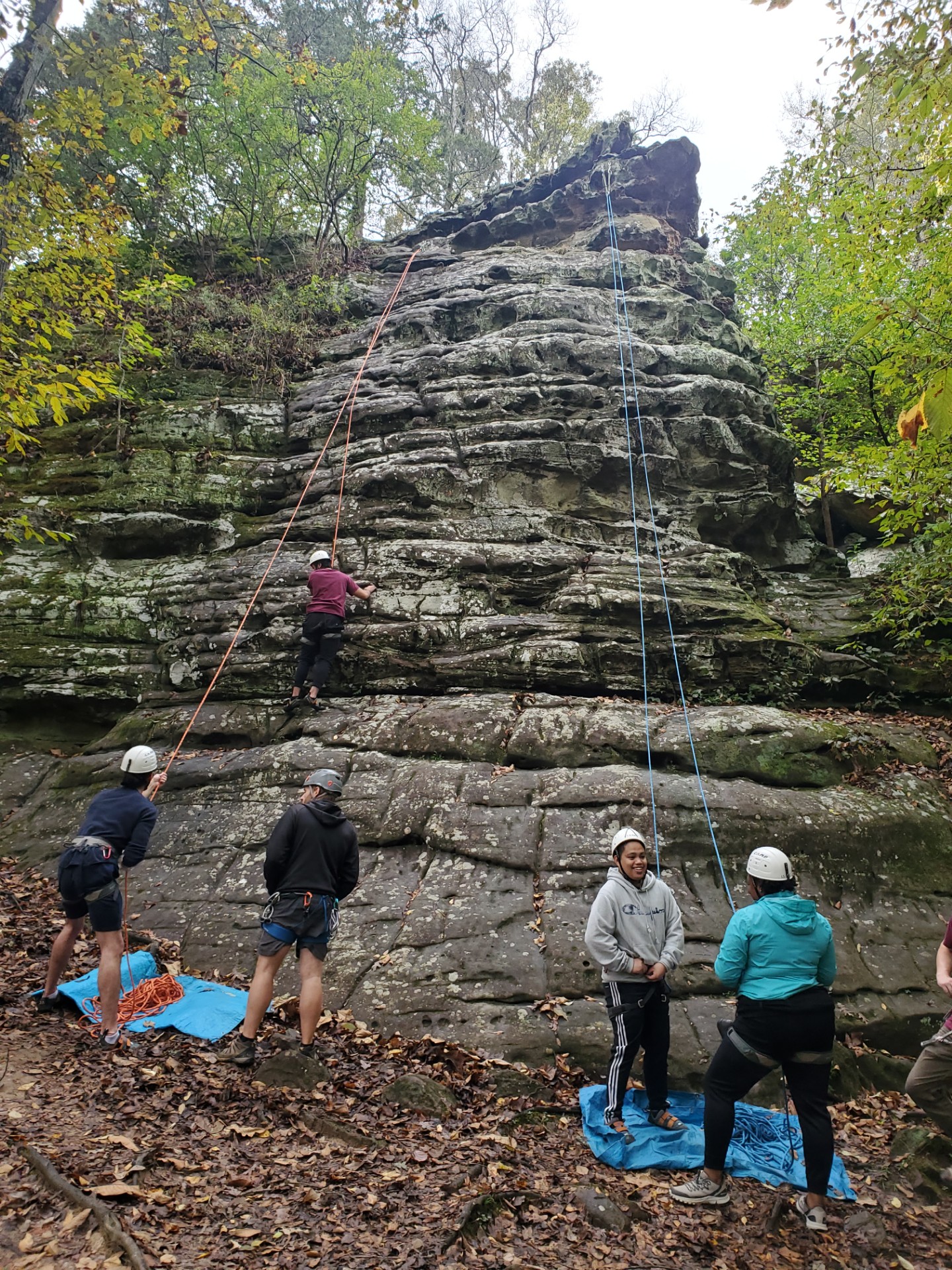 Several participants in a climbing class gather around an outdoor climbing location. 