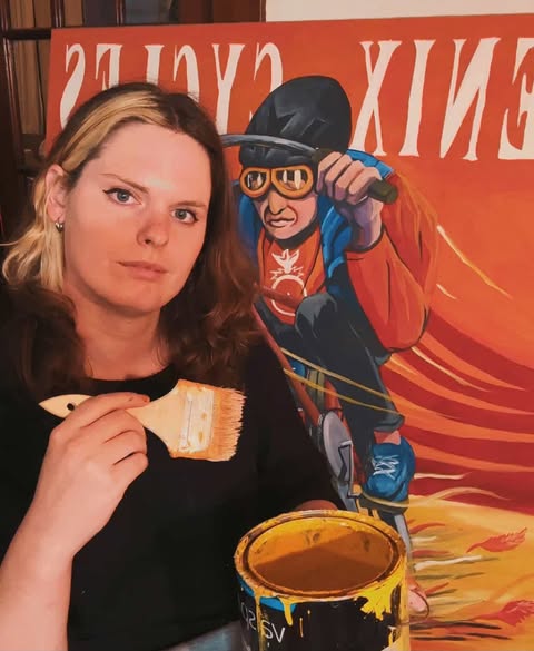 Brooke Yandle poses with a recently completed mural, a paintbrush, and a can of yellow paint. 