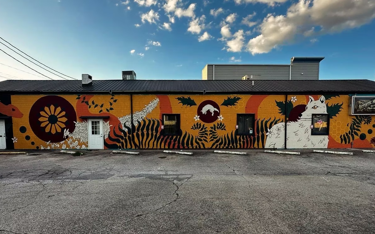 A mural on the side of a building. It has various animals and a color scheme that includes lots of yellow, red, white, and black. 