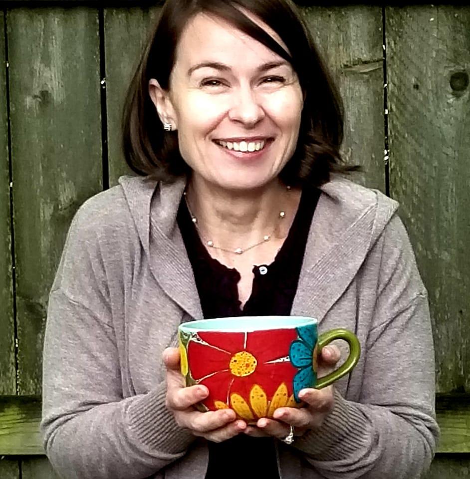 A woman holds a hand-painted, over-sized mug in both hands. She's smiling. 